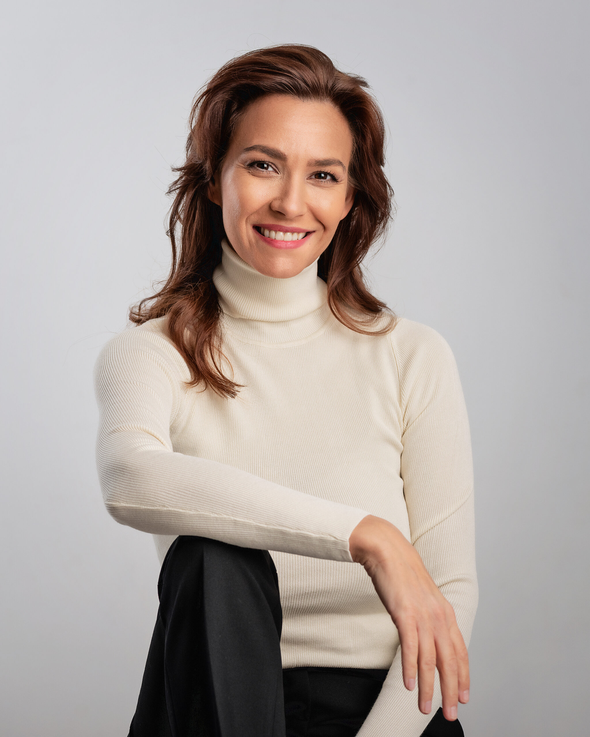 Studio portrait of a brunette haired woman wearing turtleneck sweater and cheerful smiling against isolated white background. Copy space.
